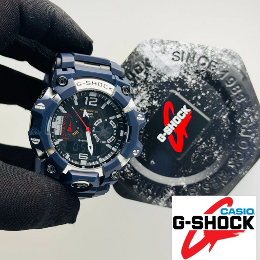 A navy blue Casio G-Shock analog watch with a black dial and silver accents, held by a hand wearing a black glove next to its branded packaging box.