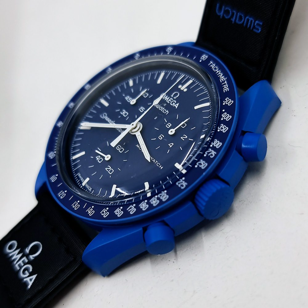 Omega Swatch automatic watch with a blue dial, blue case, and black strap, photographed on a light surface.