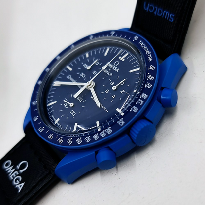 Omega Swatch automatic watch with a blue dial, blue case, and black strap, photographed on a light surface.